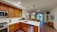 Located at 2615 Cannon Rd, #102 in Carlsbad, this single-floor residence offers a well-designed open-concept layout that seamlessly connects the kitchen, dining, and living areas. The kitchen is outfitted with warm honey-toned wood cabinetry, white countertops, and a full suite of stainless steel appliances including a range with overhead microwave, dishwasher, and a side-by-side refrigerator. Pendant lighting above the peninsula adds a refined touch, while recessed lighting and crown molding throughout contribute to a polished finish. The living area is comfortable and naturally lit, opening directly to a private outdoor patio through a sliding glass door with an arched accent window. Wood-style flooring runs through the main living spaces, while the bedrooms feature plush carpet for added comfort. Each bedroom benefits from natural light through sizable windows with outdoor views. The bathroom is spacious and clean, featuring a wood-toned vanity, wide mirror, and a separate shower area. An in-unit washer and dryer add everyday convenience. Overall, the space presents a warm, functional, and well-appointed single-level layout ideal for comfortable living in Carlsbad.
