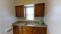 This single-floor residence offers a well-organized layout with two bedrooms and one and a half bathrooms, designed to maximize functionality and everyday comfort. The kitchen is a notable feature of the home, showcasing warm-toned wooden cabinetry with brushed nickel hardware on both the upper and lower cabinets, providing generous storage space. The countertops display a speckled granite-style surface that adds a touch of durability and visual interest. A stainless steel sink is centrally positioned beneath a window fitted with blinds, allowing natural light to brighten the workspace. The neutral wall tones throughout complement the cabinetry's warm hues, creating a cohesive and inviting atmosphere. The single-story design ensures ease of movement across the home, making it an accessible and practical living space. With its combination of ample cabinetry, natural light, and clean finishes, this residence presents a straightforward yet comfortable environment suited for everyday living.
