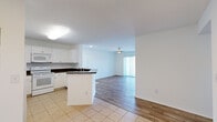 This well-maintained single-floor residence offers a clean, functional layout with a bright and inviting atmosphere throughout. The open-concept living area features wood-style laminate flooring and a ceiling fan, with a sliding glass door fitted with vertical blinds that fills the space with natural light and provides access to an outdoor view. The kitchen flows seamlessly from the living area and is equipped with white cabinetry, dark granite-style countertops, a peninsula breakfast bar, white appliances including a refrigerator, electric range, and built-in microwave, as well as light tile flooring. The bedrooms continue the wood-style laminate flooring and are bathed in natural light — one features a window with a view of surrounding greenery, while another includes a closet and direct access to the bathroom. The bathroom is well-appointed with a vanity featuring a stone-tone countertop, a large mirror with overhead lighting, tile flooring, and a walk-in shower with sliding glass doors. The space also includes a utility panel conveniently located in the kitchen area. Clean white walls and consistent finishes throughout give this residence a bright, cohesive, and move-in ready feel.