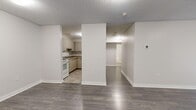 This single-floor, 3-bedroom, 1-bathroom unit offers a practical and well-organized layout designed for comfortable everyday living. The open entryway leads into two living areas finished with durable dark laminate flooring and neutral grey-white walls, creating a bright and cohesive atmosphere throughout. The kitchen is efficiently laid out with textured laminate cabinetry, granite-look countertops, a built-in dishwasher, and tile flooring — providing ample storage and counter workspace. Three hallways connect the rooms, ensuring a logical and accessible flow across the floor plan. Each of the three bedrooms features laminate flooring in warm grey tones. The generously sized primary bedroom offers a large sliding-door closet and access to the hallway. The secondary bedrooms are equally well-finished, with one featuring a window that brings in natural light and an exterior view. The full bathroom is cleanly appointed with subway-tiled tub surround, a modern vanity with an integrated sink and mirrored medicine cabinet, and neutral tile flooring. Textured ceilings are consistent throughout the unit, adding subtle architectural character. Overall, this space presents a clean, move-in-ready interior with a functional and efficient design.
