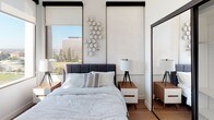 Located on the iconic Wilshire Boulevard in the heart of Los Angeles, this thoughtfully designed single-floor unit offers a clean, modern aesthetic with warm wood-tone flooring that runs seamlessly throughout the space. The open-concept layout connects the living, dining, and kitchen areas, creating a functional and inviting environment. The kitchen is well-appointed with white cabinetry fitted with matte black hardware, stainless steel appliances including a range, over-the-range microwave, dishwasher, and full-size refrigerator, complemented by light countertops and a stainless steel sink. A compact dining area features a fold-down bamboo table with seating for two, ideal for everyday use. The living room offers generous natural light through large black-framed windows with roller shades, and provides a comfortable, airy atmosphere. The bedroom is a serene retreat with expansive windows framing sweeping city views of the Los Angeles skyline and surrounding greenery, bringing abundant natural light into the room. A sleek floor-to-ceiling mirrored closet adds both function and depth. The bathroom features a full tub-shower combination with white subway tile surround and chrome fixtures. An in-unit washer is also present, adding everyday convenience to this well-curated urban residence.