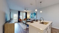 This thoughtfully designed single-floor residence offers a seamless blend of modern aesthetics and functional living. The open-concept layout connects the entryway, kitchen, dining, and living areas, creating a bright and cohesive flow throughout the main living space. Warm wood-look flooring runs throughout the common areas, complementing the soft, neutral color palette on the walls.

The kitchen is well-equipped with stainless steel appliances, sleek white cabinetry, light stone countertops, and a central island with a built-in sink — ideal for both everyday cooking and entertaining. Pendant lighting above the island adds a refined touch. The living area is generously proportioned, bathed in natural light from large windows dressed with navy curtains, and features a ceiling fan overhead.

The bedroom is a calm retreat, carpeted for comfort and illuminated by multiple windows that frame serene outdoor views. Ample natural light fills the room throughout the day. A hallway leads to the bathroom, which features wood-look flooring, a vanity with mirror, and clean, modern fixtures. The overall ambiance of the space is contemporary and welcoming, with consistent attention to detail evident in every room.