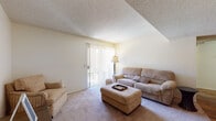 Located at 1701 N Wilmot Rd in Tucson, Arizona, this single-floor residence offers a practical and comfortable layout designed for everyday living. The living area is carpeted and filled with natural light streaming through a large sliding glass door fitted with vertical blinds, providing access to an outdoor space. A textured ceiling adds character throughout the common areas.

The kitchen is a galley-style layout featuring rich, dark wood cabinetry, dark granite-style countertops, hardwood flooring, and white appliances including a range, dishwasher, and refrigerator. A double-basin sink sits beneath a window, making the space both functional and efficient.

The bedrooms are carpeted and quietly appointed, offering a restful retreat. Each room features textured ceilings and ample space. One bedroom includes a walk-in closet with built-in shelving, while another is flanked by classic wooden nightstands and warm lamp lighting, lending a cozy ambiance.

The bathroom is accessible via a hallway and showcases hardwood flooring, a warm wood vanity with a granite-style countertop, a large mirror, and open built-in shelving for additional storage. The entry area transitions from hardwood to carpet, connecting seamlessly to the living space. Overall, the residence presents a well-maintained, cohesive interior with warm tones throughout.