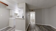 This efficiently designed single-floor unit offers a practical and comfortable layout across one bedroom, one bathroom, a living room, and a closet. The living area is finished with durable wood-look plank flooring in a warm gray tone and features a ceiling fan with a light fixture. Neutral gray walls and white baseboards throughout lend a clean, modern aesthetic. A pass-through counter connects the living space to the kitchen, which is equipped with white cabinetry and a freestanding range, making the most of the available footprint.

The bedroom continues the same wood-look flooring and neutral palette, with a ceiling fan overhead and a window fitted with blinds that allows natural light to filter in. A dedicated closet provides convenient storage. The full bathroom is finished with large-format earthy tile on both the walls and floor, surrounding a full soaking tub and shower combination with a brushed nickel fixtures. A standard toilet completes the bathroom layout.

Overall, the space presents a cohesive and tidy interior with consistent finishes throughout, offering a functional and low-maintenance living environment well-suited for individuals or couples seeking a straightforward, single-level layout.