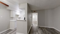 This efficiently designed single-floor unit offers a practical and comfortable layout across one bedroom, one bathroom, a living room, and a closet. The living area is finished with durable wood-look plank flooring in a warm gray tone and features a ceiling fan with a light fixture. Neutral gray walls and white baseboards throughout lend a clean, modern aesthetic. A pass-through counter connects the living space to the kitchen, which is equipped with white cabinetry and a freestanding range, making the most of the available footprint.

The bedroom continues the same wood-look flooring and neutral palette, with a ceiling fan overhead and a window fitted with blinds that allows natural light to filter in. A dedicated closet provides convenient storage. The full bathroom is finished with large-format earthy tile on both the walls and floor, surrounding a full soaking tub and shower combination with a brushed nickel fixtures. A standard toilet completes the bathroom layout.

Overall, the space presents a cohesive and tidy interior with consistent finishes throughout, offering a functional and low-maintenance living environment well-suited for individuals or couples seeking a straightforward, single-level layout.