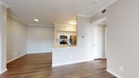 This single-floor residence offers a thoughtfully designed open-concept layout that seamlessly connects the kitchen, dining, and living areas. Rich, dark hardwood-style flooring runs throughout the main living spaces, complemented by neutral warm-toned walls and crown molding that add a polished finish to every room.

The kitchen is anchored by a wraparound peninsula with a light stone countertop and an undermount sink, providing both additional prep space and a natural boundary between the kitchen and living area. Inside the kitchen, white cabinetry is paired with stainless steel appliances, including a refrigerator, range, and built-in microwave, alongside a decorative tile backsplash. A closet pantry offers ample storage.

The living area is bright and inviting, featuring a ceiling fan, a wall-mounted mantle shelf above a fireplace, and access to the outdoors through a glass door flanked by windows that allow natural light to pour in and offer views of the surrounding greenery.

A hallway connects the main living area to the private quarters, including a bathroom finished with white tile surrounding a full soaking tub and shower combination, a vanity with white cabinetry, and matching hardwood-style flooring. The overall design is clean, modern, and functional, creating a comfortable and cohesive living environment.
