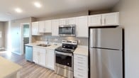 This single-floor unit offers a well-designed layout that balances functionality and modern style. The kitchen serves as a central highlight, showcasing crisp white shaker cabinetry extending to the ceiling, light quartz countertops, and a full suite of stainless steel appliances including a refrigerator, electric range, and over-the-range microwave. A large central island with pendant lighting provides additional prep space and casual seating potential, while an adjacent built-in shelving area adds convenient storage. Wood-look flooring flows throughout the main living and kitchen areas, contributing to a warm, cohesive aesthetic.

The bathroom is finished in a clean, bright palette with a white vanity featuring ample counter space, a wide mirror with overhead lighting, wood-look flooring, and a full tub and shower combination. The bedroom offers a comfortable, carpeted space with a window providing natural light and a baseboard heating unit. In-unit laundry is tucked into a dedicated area, adding everyday convenience. Neutral warm-gray wall tones and recessed lighting throughout give the space a consistently modern and move-in-ready feel.
