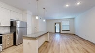 This well-appointed one-bedroom, one-bathroom unit in Leander, TX offers a thoughtfully designed single-level layout that maximizes functionality and comfort. The open-concept kitchen and living area serves as the heart of the home, anchored by a granite-topped island with elegant pendant lighting overhead. The kitchen is outfitted with crisp white upper cabinetry, warm wood-toned lower cabinets, a classic subway tile backsplash, and a full suite of stainless steel appliances including a refrigerator, range, microwave, and dishwasher. Light wood-style flooring flows throughout the main living areas, lending a bright and airy feel. The living room benefits from natural light through a glass-paneled door and an adjacent window fitted with blinds. Built-in open shelving adds a practical and stylish accent near the entryway. The bedroom features plush wall-to-wall carpet, a ceiling fan, and dual windows that invite natural light. Two closets provide generous storage, and the bathroom is finished with a wood-toned vanity, granite countertop, tile flooring, and a tiled tub-shower combination. A dedicated laundry area completes this efficient and modern living space.