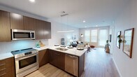 This single-floor residence offers a well-designed layout that balances modern aesthetics with practical functionality. The entryway sets an immediate tone with light wood-look flooring, a bold black slatted accent wall fitted with metal hooks for storage, and a patterned area rug that adds visual interest underfoot. A hallway connects the entry to the rest of the unit, lined with clean white walls and coordinating trim.

The open-concept kitchen and living area serves as the heart of the space. The kitchen is outfitted with rich dark wood cabinetry, quartz countertops, stainless steel appliances including a refrigerator, range, microwave, and dishwasher, and a peninsula with an undermount sink that doubles as a casual dining space. A linear pendant light anchors the kitchen zone. The living area flows seamlessly from the kitchen, featuring recessed lighting, a large window and glass door that invite natural light, and light hardwood-style flooring throughout.

The bedroom is a calm retreat with plush carpet, a ceiling fan, and a generously sized window. The bathroom showcases a patterned tile floor, dual-sink vanity with dark wood cabinetry, white quartz countertops, and a subway-tiled shower. An in-unit laundry area with a stacked washer and dryer and built-in shelving adds everyday convenience.