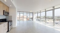 Located at 8155 Van Nuys Blvd in Panorama City, California, this modern single-floor unit showcases a sleek, open-plan design with an emphasis on natural light and contemporary finishes throughout. The expansive living area is anchored by polished concrete floors and floor-to-ceiling curtain-wall windows that wrap around the space, flooding the interior with natural light and offering sweeping views of the surrounding Panorama City streetscape, including palm trees and the San Fernando Valley skyline.

The kitchen is thoughtfully integrated into the open living area and features light wood cabinetry with clean-line hardware, a glass tile backsplash, and a full suite of stainless steel appliances including a refrigerator, electric range, built-in microwave, and dishwasher. A single-basin sink with a modern gooseneck faucet completes the functional workspace.

The bathroom offers a clean, minimalist aesthetic with white subway tile lining the walls of a soaking tub and shower combination, accented by a frameless glass sliding door and polished chrome fixtures.

Throughout the unit, the crisp white walls and smooth ceilings with recessed and flush-mount lighting contribute to an airy, contemporary ambiance. The abundance of glazing and open sightlines create a bright, loft-like atmosphere well-suited for a variety of uses.
