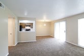 This single-floor residence offers a well-organized layout designed for comfortable everyday living. The expansive living room serves as the heart of the home, featuring plush wall-to-wall carpeting, a ceiling fan, a textured ceiling, and a tile-surround fireplace that adds a warm, inviting focal point to the space. Large windows and a sliding glass door allow abundant natural light to fill the room while providing views of the outdoors.

The galley-style kitchen is efficiently designed with rich wood cabinetry lining both sides, white appliances including an electric range and refrigerator, a double basin sink, and dark hardwood-style flooring. A window at the end of the kitchen brings in additional natural light.

The bedrooms are generously sized, each finished with soft carpeting and neutral warm-toned walls. Several rooms feature large windows fitted with blinds, and at least one bedroom includes a closet with built-in shelving. The full bathroom is neatly appointed with a wood-toned vanity, white countertop, a large mirror, and a tub and shower combination enclosed by a sliding frosted glass door. The bathroom area also includes a separate vanity space with additional storage and a window for natural light. Throughout the residence, clean white trim and a consistent neutral palette create a cohesive, understated aesthetic.
