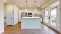 This efficiently designed 1-bedroom, 1-bathroom unit offers a thoughtful layout across a single floor, making excellent use of every square foot. The open-concept kitchen and living area serves as the heart of the space, featuring wood-look vinyl flooring, recessed lighting, and large windows that invite natural light and offer views of the surrounding neighborhood. The kitchen is well-appointed with white shaker-style cabinetry, warm wood lower cabinets, a white quartz countertop, a subway tile backsplash, stainless steel appliances including a refrigerator, range, and microwave, and a central island with pendant lighting above.

The living area provides a clean, open canvas with neutral walls and durable flooring. A dedicated hallway leads to the private bedroom, which features soft wall-to-wall carpeting, a ceiling fan, and access to a walk-in closet with built-in shelving. The full bathroom includes a wood-toned vanity with a white countertop, a soaking tub and shower combination, tile surround, and matte black hardware accents. A hallway nook accommodates a stacked Whirlpool washer and dryer, adding everyday convenience directly within the unit.