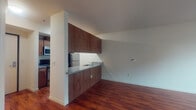 Located on the third floor at 305 E Mill Plain Blvd in Vancouver, Washington, this apartment offers a well-designed single-level layout that balances functionality and modern style. The open-concept living and kitchen area is anchored by rich, warm hardwood-style flooring that extends throughout the main living spaces, creating a cohesive and inviting atmosphere.

The kitchen features a peninsula-style layout with walnut-toned cabinetry, granite-style countertops, and stainless steel appliances including a refrigerator, microwave, and an electric range. Upper cabinetry provides generous storage, and the peninsula serves as a natural divider between the kitchen and the open living area.

The bedroom is carpeted for comfort, bathed in natural light from a large window overlooking the surrounding urban streetscape, and includes a wall-mounted climate control unit. An additional room with hardwood-style flooring and a large window offers flexible use as a second bedroom, office, or den.

The bathroom is well-appointed with tile flooring, a full tiled tub-and-shower surround, a toilet, and a dual-sink vanity topped with granite-style countertops and rich wood cabinetry. A large mirror and overhead lighting complete the space. A washer and dryer are also included within the unit, adding everyday convenience to this thoughtfully designed Vancouver residence.