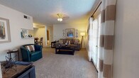 Located at 8301 N Council Rd in Oklahoma City, Oklahoma, this single-floor residence offers a comfortable and well-appointed layout designed for everyday living. The living room serves as the heart of the home, featuring plush wall-to-wall carpeting, a textured ceiling, and a ceiling fan with light fixture. Large sliding glass doors dressed with striped curtains flood the space with natural light and provide access to the outdoors, creating an open and inviting atmosphere. The living area flows naturally into a dining space adjacent to the kitchen, which is equipped with warm wood cabinetry, a dishwasher, refrigerator, and sink — all thoughtfully arranged for efficient use. The bedrooms are generously proportioned, each with soft carpeting, ceiling fans, and windows that bring in natural light. The primary bedroom benefits from direct access to a private bathroom and a walk-in closet, while additional bedroom space offers ample room for storage and comfort. The full bathroom features a tub-shower combination with tile surround, a toilet, and clean, neutral finishes throughout. Overall, the residence presents a warm, functional interior with a neutral color palette and practical design elements suited for comfortable daily living.