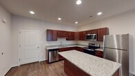 Located at 6343 Logans Ln in Lynchburg, Virginia, this single-floor residence offers a clean, modern design with thoughtfully appointed interiors throughout. The kitchen serves as a standout feature, showcasing rich dark cabinetry, light granite countertops, a central island for additional prep and dining space, and a full suite of stainless steel appliances including a refrigerator, electric range, built-in microwave, and dishwasher. Recessed lighting illuminates the space, and durable wood-look flooring ties the kitchen and open living areas together seamlessly. The living and dining areas are open and airy, benefiting from natural light provided by windows with blinds, neutral wall tones, and consistent wood-look flooring that enhances the sense of space. The bedrooms feature soft carpeting, natural light from windows, and ample room for furnishings. A generously sized walk-in closet with wire shelving provides excellent storage capacity. The bathroom is efficiently designed, featuring a full tub-shower combination with a curved curtain rod, and clean, neutral finishes. Throughout the home, the overall aesthetic is contemporary and move-in ready, with a neutral color palette that offers versatility for personalization.