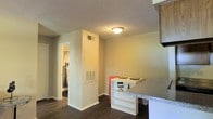This single-floor residence offers a practical and efficient layout designed to maximize its available space. The main living area features rich, dark hardwood-style flooring that runs throughout, providing a warm and cohesive look across the unit. The living room is a comfortable space, accommodating a sofa and a glass-top coffee table, and is accented with decorative wall art that adds a touch of personality to the room.

Adjacent to the living area, a compact dining nook features a white bar-style counter with granite-look surface, paired with orange bar stools — a functional and casual spot for dining or working. A built-in column housing HVAC venting serves as a subtle architectural divider between the living and dining zones, keeping utilities neatly integrated into the structure.

The textured popcorn ceiling and flush-mount ceiling light fixtures are consistent throughout the space, lending a uniform finish. A hallway visible from the main area leads to the bathroom, which includes a toilet and tub, offering straightforward functionality. A second hallway with a curtained entrance suggests additional room access.

Overall, the space presents a straightforward, no-frills layout with a clean, move-in-ready feel, suitable for those seeking a manageable and practical living environment.