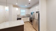 Located at 1000 Infinity Dr in Maryville, Tennessee, this single-floor residence offers a clean, modern aesthetic with consistent wood-look flooring and crisp white walls throughout. The open-concept kitchen is a standout feature, equipped with stainless steel appliances including a refrigerator, range, and microwave, complemented by white shaker-style cabinetry, granite countertops, and a dark-based center island with pendant lighting overhead. A window above the sink brings in natural light, enhancing the bright and functional layout. The kitchen flows seamlessly into the living area, which provides an open and airy feel. Each bedroom is generously sized, featuring ceiling fans with light fixtures and windows with blinds that allow for natural light and outdoor views. The primary bathroom includes a dual-sink vanity with granite countertops, white cabinetry, and a large mirror with overhead lighting. A walk-in closet is accessible directly from the bathroom, offering ample storage. Additional bathrooms follow the same refined design language. Clean lines, neutral tones, and quality finishes define the overall ambiance of this well-designed residence.