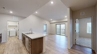 This thoughtfully designed 2-bedroom, 3-bathroom single-floor residence offers a functional and modern living experience. The open-concept kitchen and living area serves as the heart of the home, featuring light hardwood-style flooring, vaulted ceilings with recessed lighting, and a large center island with a marble-look quartz countertop and undermount sink. Rich walnut-toned cabinetry lines the kitchen walls, complemented by a full suite of stainless steel appliances including a refrigerator, range, and microwave. Sliding glass doors open from the living area to a private balcony, flooding the space with natural light and providing pleasant outdoor views of surrounding trees and landscaping. Both bedrooms are carpeted and include ceiling fans and windows that bring in ample natural light. The primary bedroom offers comfortable proportions and access to a dedicated closet with built-in shelving and hanging rods. The three bathrooms are finished with quartz-topped vanities and warm wood cabinetry; one features a walk-in shower with built-in shelving, while another includes a full soaking tub. A dedicated laundry room accommodates a full-size washer and dryer with overhead shelving for added storage. Two closets throughout the home provide practical organization solutions.