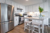Located at 2613 Atlantic Ave in Virginia Beach, VA, this single-floor coastal retreat is thoughtfully designed with a bright, airy aesthetic that reflects its beachside surroundings. The modern kitchen is a standout feature, boasting floor-to-ceiling white shaker cabinetry, a herringbone tile backsplash, stainless steel appliances including a French door refrigerator and gas range, quartz countertops, and a peninsula with bar seating — ideal for casual dining and entertaining. Light hardwood flooring flows throughout the space, enhancing the open, breezy feel. The primary bedroom is bathed in natural light from large windows offering outdoor views, and is decorated in soft aqua and yellow coastal tones. The second bedroom carries a similarly serene palette with neutral tones, warm wood accents, and tasteful coastal artwork. Both bathrooms are finished with classic white subway tile, black-and-white mosaic tile flooring, white vanities with quartz counters, and illuminated mirrors, lending a clean, timeless look. The overall ambiance of the space is cohesive and inviting, with a coastal design theme carried consistently from room to room through soft color palettes, natural materials, and carefully chosen finishes.