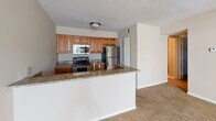 Located at 2274 Ashley River Road in Charleston, SC, Unit 513 is a single-floor residence offering a well-designed layout with functional living spaces throughout. The kitchen is a standout feature, equipped with warm-toned wooden cabinetry, granite countertops, stainless steel appliances including a refrigerator, range, and over-the-range microwave, and a double sink. A peninsula counter with granite surfaces connects the kitchen to the adjoining living area, creating an open, cohesive flow between spaces. The living room is generously sized, featuring plush wall-to-wall carpeting, a ceiling fan with light fixture, a classic fireplace with a white surround, and a glass door that opens to an outdoor balcony, allowing natural light to fill the room. The bedroom is comfortably proportioned with carpet flooring, neutral-toned walls, and a window fitted with blinds that provide natural light. The bathroom includes a granite-topped vanity with a vessel sink and rich wood cabinetry, complemented by tile flooring, and a full tub-shower combination. Textured ceilings are consistent throughout the unit, adding a classic architectural detail to each room. The overall ambiance is warm and inviting, with neutral tones providing a versatile backdrop throughout.
