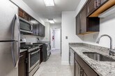 Located at 999 Hidden Lake Dr in North Brunswick, NJ, this single-floor residence offers a well-designed layout with consistent hardwood flooring flowing throughout the living areas and bedrooms. The neutral gray and white color palette creates a clean, cohesive aesthetic across the space.

The kitchen is equipped with dark espresso cabinetry, granite countertops, a stainless steel undermount sink with a pull-down faucet, and a stainless steel dishwasher, providing a functional and polished workspace. A dedicated laundry area houses a full-size Electrolux front-loading washer with overhead cabinetry for additional storage.

The living area is generously sized and filled with natural light, featuring sliding glass doors that open to an enclosed balcony overlooking lush greenery — a notable outdoor extension of the living space. Bedrooms are well-proportioned with ample natural light from multiple windows and include closets with built-in shelving systems. One bedroom connects to a bathroom with dark vanity cabinetry and a large mirror.

A walk-in closet with shelving is accessible from the primary bathroom area, adding practical storage. Throughout, white trim and doors complement the warm hardwood floors, giving the space a bright, welcoming character.