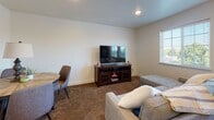 This thoughtfully designed single-floor unit offers a bright and functional open-concept layout that seamlessly connects the living area and kitchen. Light wood-look flooring runs throughout the main living spaces, complementing the clean white walls and recessed lighting that keep the interior feeling fresh and modern. Large windows with white blinds invite ample natural light and offer pleasant outdoor views of surrounding greenery.

The kitchen is a standout feature, showcasing rich wood-toned cabinetry with sleek hardware, granite-style countertops, and a full suite of black appliances including a refrigerator, electric range, microwave, and dishwasher. A hallway leads from the kitchen into the private areas of the unit.

The living area provides generous space for comfortable furnishings and opens to a dining area, making it well-suited for both relaxing and entertaining. Soft carpet flooring transitions the space into the bedrooms, adding warmth underfoot.

The primary bedroom features an open walk-in closet area, while the second bedroom benefits from dual windows and a closet for ample storage. Both rooms are carpeted and finished with the same neutral palette found throughout the unit.

The bathroom is well-equipped with a wood-toned vanity, granite-style countertop, large mirror, and light flooring, maintaining the cohesive modern aesthetic of the entire space.