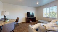 This thoughtfully designed single-floor unit offers a bright and functional open-concept layout that seamlessly connects the living area and kitchen. Light wood-look flooring runs throughout the main living spaces, complementing the clean white walls and recessed lighting that keep the interior feeling fresh and modern. Large windows with white blinds invite ample natural light and offer pleasant outdoor views of surrounding greenery.

The kitchen is a standout feature, showcasing rich wood-toned cabinetry with sleek hardware, granite-style countertops, and a full suite of black appliances including a refrigerator, electric range, microwave, and dishwasher. A hallway leads from the kitchen into the private areas of the unit.

The living area provides generous space for comfortable furnishings and opens to a dining area, making it well-suited for both relaxing and entertaining. Soft carpet flooring transitions the space into the bedrooms, adding warmth underfoot.

The primary bedroom features an open walk-in closet area, while the second bedroom benefits from dual windows and a closet for ample storage. Both rooms are carpeted and finished with the same neutral palette found throughout the unit.

The bathroom is well-equipped with a wood-toned vanity, granite-style countertop, large mirror, and light flooring, maintaining the cohesive modern aesthetic of the entire space.