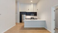 Located in Silverdale, WA, this well-appointed 2-bedroom, 2-bathroom residence offers a thoughtfully designed single-floor layout with modern finishes throughout. The open-concept living, dining, and kitchen area serves as the heart of the home, featuring light wood-look flooring, soaring ceilings, and large windows and a glass door that open to a private balcony with tranquil views of surrounding trees. The kitchen is a standout, showcasing sleek dark cabinetry that reaches toward the ceiling, a crisp white waterfall-edge island, stainless steel appliances including a gas range and refrigerator, and stylish pendant lighting. The living area is further enhanced by a wall-mounted mini-split unit for climate control. Both bedrooms are finished with plush carpet and feature generous closet space, including a walk-in closet with built-in shelving in the primary suite. The bedrooms offer peaceful wooded views through large windows, with notably tall ceilings adding an airy feel. The bathrooms are finished with dark vanity cabinetry, white countertops, and modern fixtures. Additional conveniences include in-unit laundry and multiple closets for ample storage throughout.