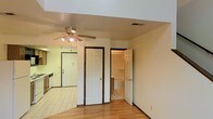 This two-floor space offers a practical and straightforward layout designed for comfortable everyday living. The main living area features warm hardwood flooring that transitions into tile in the adjacent kitchen zone, creating a clear visual distinction between spaces. A ceiling fan with an integrated light fixture is centrally positioned overhead, providing both airflow and ambient lighting throughout the room.

The space includes a closet with a classic six-panel door, offering convenient built-in storage. An open doorway leads to a bathroom, which is finished with light-colored tile flooring and features a bathtub, maintaining a clean and functional aesthetic consistent with the rest of the space.

The kitchen area is visible toward the rear, finished in coordinating tile flooring and equipped with standard appliances including a dishwasher. A door at the back of the kitchen provides additional access, likely to an exterior entry point.

Throughout the space, neutral wall tones in soft beige create a calm, versatile backdrop that works well with a variety of furnishing styles. The overall layout is efficient, with each area flowing naturally into the next. Spanning two floors, this space provides ample room for a range of uses, balancing practicality with a welcoming, livable atmosphere.