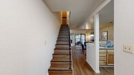 This two-story, 2-bedroom, 2-bathroom home in Fremont, CA (94555) offers a thoughtfully organized layout spread across two floors. The main level features an inviting entrance that opens to a living room anchored by a striking tile-surround fireplace and sliding glass doors leading to a private outdoor patio, allowing natural light to fill the space. Warm hardwood-style flooring runs throughout the main level, complementing the open feel. The adjacent dining area features a pendant light fixture and a pass-through counter connecting seamlessly to the kitchen, which is equipped with stainless steel appliances including a range, microwave, and refrigerator, along with light wood cabinetry and a stacked in-unit washer and dryer. Upstairs, the generously sized primary bedroom includes a sliding glass door opening to a private balcony with outdoor views, a mirrored closet, and carpeted flooring. The second bedroom is well-proportioned and comfortably appointed. Both bathrooms are functional and clean, with the upper bathroom featuring a combined tub and shower with frosted glass enclosure and warm wood vanity cabinetry. A staircase with dark wood treads and a metal railing connects the two floors, adding an architectural focal point to the home's interior.