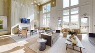 Located in Vestavia Hills, Alabama, this designer clubhouse is a single-floor community gathering space that masterfully blends Southern charm with contemporary elegance. The interior is anchored by dramatically soaring double-height ceilings clad in warm, light-toned wood paneling that lends a natural, inviting atmosphere throughout. Expansive floor-to-ceiling windows flood the space with abundant natural light and offer views of the surrounding community. Wide-plank hardwood flooring runs seamlessly across the open layout, tying the various zones together cohesively. The main lounge area features a fireplace with a herringbone tile surround, curated seating arrangements, and a wall-mounted television, creating an ideal setting for relaxed social gatherings. A bar area with counter seating, pendant lighting, and decorative plate wall art adds a stylish focal point. A dedicated reception zone with a bold dark ceiling, pendant lights, and blue upholstered seating provides a striking contrast to the brighter lounge. A cozy built-in banquette nook with leather bench seating and a statement pendant light offers an intimate retreat. The space is further enriched by a hand-lettered wall mural reading "Sweet Home Alabama, where the skies are so blue," reinforcing the locale's distinctive character.