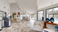 This single-floor community space makes a strong first impression with its dramatic vaulted ceilings that soar overhead, amplifying the sense of openness throughout. Large format stone-look tile flooring flows seamlessly across the entire space, unifying each area with a clean, cohesive aesthetic. Natural light pours in through an abundance of oversized windows and glass entry doors, creating a bright and airy atmosphere throughout the day.

The welcoming entry lounge features an elegant chandelier as a focal point, complemented by comfortable seating arrangements ideal for relaxing or socializing. Large windows frame views of the outdoor pool area, bringing the outdoors in. A service and business area with a pass-through window provides practical functionality within the open layout.

The kitchen is a standout feature, designed with crisp white shaker cabinetry, granite countertops, a subway tile backsplash, and stainless steel appliances. A generous breakfast bar with seating for multiple guests encourages casual gatherings, while pendant lighting adds a refined touch. A dedicated full kitchen with additional white cabinetry and granite counters offers ample prep space and natural light from a window overlooking the exterior.

Throughout, the neutral white and gray palette, high ceilings, and thoughtful design elements combine to create a polished, inviting environment suited for community activities and everyday use.