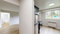 Located at 11405 132 St in Edmonton, Alberta, this 2-bedroom, 1-bathroom unit offers a practical and modern single-floor layout with thoughtfully updated finishes throughout. Light wood laminate flooring flows continuously across all rooms, creating a cohesive and bright interior atmosphere.

The living area is generously proportioned, featuring large windows that frame views of lush greenery outside, allowing abundant natural light to fill the space. Radiator heating units are positioned beneath the windows throughout the unit. The kitchen is a standout feature, designed in a galley style with dark wood-grain cabinetry lining both walls, grey stone countertops, a tile backsplash, a stainless steel sink, and stainless steel appliances including a range and refrigerator. A built-in closet with shelving is accessible directly from the kitchen.

The primary bedroom is spacious, offering ample room for furnishings, while the second bedroom also provides a comfortable footprint with a closet and a window overlooking the outdoors. Both bedrooms are finished with the same neutral grey tones and light wood flooring found throughout. The bathroom is clean and modern, featuring a full soaker tub with a marble-style tiled surround, a dark vanity with a grey countertop, and wood-tone flooring. Two hallways and a dedicated entrance complete the layout.
