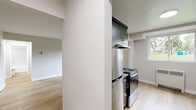 Located at 11405 132 St in Edmonton, Alberta, this 2-bedroom, 1-bathroom unit offers a practical and modern single-floor layout with thoughtfully updated finishes throughout. Light wood laminate flooring flows continuously across all rooms, creating a cohesive and bright interior atmosphere.

The living area is generously proportioned, featuring large windows that frame views of lush greenery outside, allowing abundant natural light to fill the space. Radiator heating units are positioned beneath the windows throughout the unit. The kitchen is a standout feature, designed in a galley style with dark wood-grain cabinetry lining both walls, grey stone countertops, a tile backsplash, a stainless steel sink, and stainless steel appliances including a range and refrigerator. A built-in closet with shelving is accessible directly from the kitchen.

The primary bedroom is spacious, offering ample room for furnishings, while the second bedroom also provides a comfortable footprint with a closet and a window overlooking the outdoors. Both bedrooms are finished with the same neutral grey tones and light wood flooring found throughout. The bathroom is clean and modern, featuring a full soaker tub with a marble-style tiled surround, a dark vanity with a grey countertop, and wood-tone flooring. Two hallways and a dedicated entrance complete the layout.