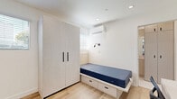 Located at 2601 S Hoover St in Los Angeles, CA, this efficiently designed studio unit offers a well-planned single-floor layout that maximizes every square foot. The space features light-toned hardwood flooring throughout, crisp white walls, and recessed lighting that contribute to a bright, clean aesthetic.

The sleeping area includes a platform bed with integrated under-bed storage drawers and a large two-door wardrobe with sleek black hardware, providing ample storage without sacrificing floor space. A wall-mounted mini-split HVAC unit ensures year-round climate control, and an adjustable wall-mounted reading light adds functional detail.

A dedicated workspace features a compact white desk with a wall-mounted flat-screen television above it, ideal for studying or remote work. The kitchen is well-appointed with white cabinetry, a white subway tile backsplash, stainless steel appliances including a refrigerator, gas range, microwave, and dishwasher, as well as a single-basin sink beneath a window that brings in natural light.

The bathroom is finished with marble-look tile flooring and includes a glass-door shower stall with built-in shelving, a toilet, and a vanity. The overall design is modern, functional, and cohesive, making efficient use of the available space.