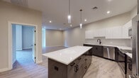 Located at 125 Warren St in Boston, MA, this thoughtfully designed single-floor residence showcases a clean, modern aesthetic with high-quality finishes throughout. The open-concept kitchen is a standout feature, boasting two-tone cabinetry with sleek white upper cabinets and dark lower cabinets, white quartz countertops, a tile backsplash, stainless steel appliances, a matte black faucet, and a large center island illuminated by stylish pendant lighting. Light wood-tone flooring flows seamlessly throughout the living areas, complementing the neutral warm-gray wall tones and creating a bright, cohesive ambiance. The spacious living area offers generous room for furnishing and entertaining. The bedrooms are well-proportioned, filled with natural light from multiple windows, and include dedicated closet space. The primary bathroom features a glass-enclosed marble-tile walk-in shower, large-format tile flooring, a white vanity with black hardware, and a frameless mirror. A secondary half bath is finished with a clean white vanity, tile flooring, and matching black fixtures. In-unit laundry is also present. Recessed lighting throughout ensures a bright and inviting atmosphere. This residence offers a modern, move-in ready living experience in Boston.