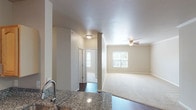 This single-story residence offers a well-designed layout that balances open communal spaces with comfortable private areas. The kitchen serves as a functional centerpiece, featuring granite countertops, a double stainless steel sink, light wood cabinetry with arched door detailing, stainless steel appliances including a refrigerator and microwave, and track lighting overhead. The kitchen flows naturally into a dining area and adjoining living space, both finished with rich, dark hardwood-style flooring that adds warmth throughout.

The living area is generously proportioned, with a ceiling fan overhead and windows that invite natural light. An arched architectural detail connects to a secondary carpeted space, adding a distinctive design element to the interior. The bedrooms are carpeted for comfort, each featuring ceiling fans, natural light from windows with blinds, and closet storage. Crown molding accents one of the bedrooms, contributing a refined finish.

Two full bathrooms mirror each other in design, each offering a granite-topped vanity with a light wood cabinet base, a tub-shower combination with tiled surround, and hardwood-style flooring. The neutral color palette and consistent finishes throughout create a cohesive and clean aesthetic across the entire space.