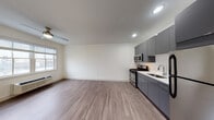 Located at Village Place in Bay Shore, NY, this two-floor residence offers a thoughtfully designed layout that balances modern finishes with functional living. The main level features an open-plan living and kitchen area finished with smooth hardwood-style flooring. The kitchen is equipped with sleek, dark gray high-gloss cabinetry extending to the ceiling, a full suite of stainless steel appliances including a gas range, over-the-range microwave, and refrigerator, complemented by a clean white countertop and undermount sink. Recessed lighting and a ceiling fan contribute to a bright, comfortable atmosphere, while a window allows natural light to fill the space. A utility area with an electrical panel and access door is tucked conveniently nearby. A staircase with metal railings connects the two floors, with a spacious walk-in closet featuring wire shelving located on the lower level. The upper floor hosts a generously sized bedroom with plush carpeting, a ceiling fan, wall-unit HVAC, and windows with blinds that invite natural light. The full bathroom is finished in neutral tones and includes a large sliding-glass enclosed shower, a white vanity, and tile flooring, offering a clean and contemporary feel throughout.