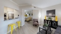 Located at 11355 Richmond Ave in Houston, TX, this single-floor residence offers a cohesive and modern interior design. The open-concept living and dining area is finished with light wood-look flooring, crown molding, and large windows dressed with gray grommet curtains that allow ample natural light. A kitchen pass-through with a breakfast bar connects seamlessly to the living space, creating an inviting flow for everyday living and entertaining.

The kitchen is outfitted with crisp white shaker-style cabinetry, granite-look countertops, a classic subway tile backsplash, and stainless steel appliances, including a range with an overhead ventilation hood and a double-basin sink. The adjacent dining area is bright and open, enhanced by a mirrored accent wall that adds depth to the space.

The bedrooms feature plush carpeting, generous natural light from windows with blinds and drapes, and ample closet space — one bedroom showcasing floor-to-ceiling mirrored sliding closet doors. The bathrooms are clean and functional, with white cabinetry, granite-look countertops, wood-look tile flooring, and a shower-tub combination. The neutral warm-gray palette carried throughout the home creates a calm, cohesive ambiance.