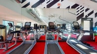 Located at 5415 Turtle Station in Westerville, Ohio, this single-floor fitness center is designed to deliver a dynamic and motivating workout environment. The space is defined by its striking aesthetic, featuring bold black-and-white geometric graphic murals along the upper walls, vivid red carpet flooring in the primary workout zones, and expansive floor-to-ceiling mirrors that amplify the sense of space and allow exercisers to monitor their form.

The cardio area is well-equipped with multiple treadmills and stationary bikes, each outfitted with individual media screens. Large garage-style glass doors line one side of the facility, flooding the interior with natural light and offering open views to the outdoor area beyond. Oversized industrial ceiling fans maintain airflow throughout the high-vaulted ceiling space.

A dedicated functional training zone features a multi-station cable and resistance rig, TRX suspension trainers, battle ropes, plyometric boxes, and a BOSU balance trainer, catering to a wide range of training styles. The strength training section includes selectorized weight machines, a cable pulldown station, adjustable benches, and a full rack of dumbbells positioned along a wall of large windows that provide abundant natural light and neighborhood views. The overall ambiance is energetic, modern, and purpose-built for comprehensive fitness.
