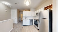 Located at 5000 Mountain Springs Dr in Nashville, TN, this two-floor residence offers a well-organized layout across two levels connected by carpeted staircases with clean white railings. The upper floor comprises the majority of the living space, while the lower entry level provides a compact transitional area.

The kitchen is a standout feature, designed with white shaker-style cabinetry, a classic subway tile backsplash, and light wood-look flooring. It is fully equipped with a stainless steel refrigerator, electric range, over-the-range microwave, and dishwasher. A built-in wine rack adds a charming decorative touch above the upper cabinetry.

The bathroom is finished with light wood-look flooring and includes a single-sink vanity with white cabinetry, a large mirror, and a combined tub and shower with tiled surround. Brushed nickel fixtures and grab bars complete the functional and clean aesthetic.

The living area features neutral carpet, a ceiling fan with light fixture, and windows that allow natural light to fill the space. Two closets provide practical storage throughout the unit. The overall interior palette of warm neutrals, white trim, and light flooring creates a bright, cohesive, and move-in-ready environment.