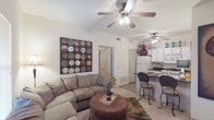 This single-story residence offers a functional and cohesive layout that connects the main living areas with ease. The living room serves as the central gathering space, featuring vaulted ceilings equipped with a ceiling fan, neutral carpet flooring, and natural light provided by a window near the front entry. A large sectional sofa anchors the room, which opens directly toward the kitchen and dining area.

The kitchen is designed for efficiency, featuring white cabinetry extending to the ceiling, dark granite-style countertops, white appliances including a refrigerator, electric range, and built-in microwave. A galley-style configuration maximizes counter and storage space, with tile flooring and a closet pantry tucked along one wall. A breakfast bar with seating connects the kitchen to the living area, creating an open and sociable atmosphere.

Both bedrooms are carpeted and include ceiling fans, windows that allow natural light, and sufficient space for standard furnishings. The bedrooms maintain a calm, neutral palette consistent with the rest of the unit. The bathroom features tile flooring, a white vanity with an undermount sink, a framed mirror, and tiled accent detailing, offering a clean and straightforward design.