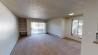 Located at 38680 Hastings St in Fremont, California, this single-floor unit offers a functional and straightforward layout designed for comfortable everyday living. The living area is generously sized, featuring wall-to-wall carpeting, a textured ceiling, and a sliding glass door that opens onto a private balcony with a latticed railing, allowing natural light to flow in and providing views of the surrounding greenery. Built-in shelving and a wall-mounted unit add practical storage and display space to the living room. Baseboard heating is present throughout the carpeted areas, ensuring efficient climate control. The kitchen is arranged in a galley style, featuring white cabinetry, laminate countertops, a stainless steel sink, and white appliances including a range and refrigerator. A pass-through window connects the kitchen to the adjacent living space, enhancing the open feel. Wood-look flooring runs through the kitchen and bathroom areas, providing a clean contrast to the carpeted rooms. The bedroom is well-proportioned with natural light from a window framing outdoor tree views. The bathroom includes a vanity with under-cabinet storage, a mirror, and a separate water closet with a bathtub and toilet. A dedicated closet area provides additional storage near the bathroom entry.