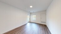 This thoughtfully designed single-floor unit offers a clean, modern aesthetic throughout its efficiently organized layout. The living room is a bright, open space featuring rich hardwood-style flooring, crisp white walls, recessed lighting, and multiple windows — including a glass-paned door — that invite abundant natural light and outdoor views of lush greenery. The room's generous proportions provide a welcoming and versatile living area.

The kitchen is equipped with gray shaker-style cabinetry, granite-look countertops, and a stainless steel dishwasher, offering a contemporary and functional workspace. Conveniently tucked nearby is a dedicated laundry area with a full-size stacked washer and dryer unit.

The bedroom is a comfortable, well-proportioned retreat finished with plush wall-to-wall carpeting and a window that frames outdoor views, creating a calm and restful atmosphere. An adjoining walk-in closet features wire shelving and hanging rods, providing ample storage.

The bathroom completes the layout, and a dedicated closet adds further organizational utility. Throughout the unit, consistent white walls, clean trim work, and a neutral color palette contribute to a bright, move-in-ready ambiance that is both practical and polished.