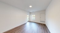 This thoughtfully designed single-floor unit offers a clean, modern aesthetic throughout its efficiently organized layout. The living room is a bright, open space featuring rich hardwood-style flooring, crisp white walls, recessed lighting, and multiple windows — including a glass-paned door — that invite abundant natural light and outdoor views of lush greenery. The room's generous proportions provide a welcoming and versatile living area.

The kitchen is equipped with gray shaker-style cabinetry, granite-look countertops, and a stainless steel dishwasher, offering a contemporary and functional workspace. Conveniently tucked nearby is a dedicated laundry area with a full-size stacked washer and dryer unit.

The bedroom is a comfortable, well-proportioned retreat finished with plush wall-to-wall carpeting and a window that frames outdoor views, creating a calm and restful atmosphere. An adjoining walk-in closet features wire shelving and hanging rods, providing ample storage.

The bathroom completes the layout, and a dedicated closet adds further organizational utility. Throughout the unit, consistent white walls, clean trim work, and a neutral color palette contribute to a bright, move-in-ready ambiance that is both practical and polished.