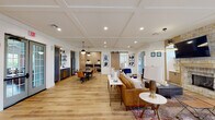 Located at 2437 Promenade Blvd in Montgomery, Alabama, this thoughtfully designed single-floor amenity space blends modern aesthetics with warm, inviting details throughout its open layout. Light hardwood flooring flows seamlessly across the entire space, unifying each distinct area while enhancing the sense of openness.

The main lounge area serves as a central gathering point, anchored by a striking floor-to-ceiling stone fireplace topped with a wall-mounted television. Comfortable leather seating, accent chairs, and layered rugs create an inviting atmosphere suited for relaxed socializing. A coffered ceiling with recessed lighting adds architectural refinement overhead.

Adjacent to the lounge, a spacious dining area features a large dark wood table surrounded by cognac leather chairs, illuminated by globe pendant lights. The kitchenette nearby is outfitted with navy blue cabinetry, subway tile backsplash, open shelving, and full-sized appliances, making it well-equipped for gatherings.

A charming built-in banquette nook with shiplap walls and a circular pendant light offers an intimate seating option near exterior French doors. A sliding barn door adds a rustic-modern touch connecting spaces. The billiards room, visible through an open archway, provides additional entertainment with generous natural light from surrounding windows.