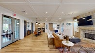 Located at 2437 Promenade Blvd in Montgomery, Alabama, this thoughtfully designed single-floor amenity space blends modern aesthetics with warm, inviting details throughout its open layout. Light hardwood flooring flows seamlessly across the entire space, unifying each distinct area while enhancing the sense of openness.

The main lounge area serves as a central gathering point, anchored by a striking floor-to-ceiling stone fireplace topped with a wall-mounted television. Comfortable leather seating, accent chairs, and layered rugs create an inviting atmosphere suited for relaxed socializing. A coffered ceiling with recessed lighting adds architectural refinement overhead.

Adjacent to the lounge, a spacious dining area features a large dark wood table surrounded by cognac leather chairs, illuminated by globe pendant lights. The kitchenette nearby is outfitted with navy blue cabinetry, subway tile backsplash, open shelving, and full-sized appliances, making it well-equipped for gatherings.

A charming built-in banquette nook with shiplap walls and a circular pendant light offers an intimate seating option near exterior French doors. A sliding barn door adds a rustic-modern touch connecting spaces. The billiards room, visible through an open archway, provides additional entertainment with generous natural light from surrounding windows.
