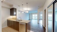 Located at 905 Southdale Rd W in London, Ontario, this well-appointed one-bedroom, one-bathroom unit offers a thoughtfully designed open-concept layout across a single floor. The kitchen is a standout feature, showcasing rich dark-brown cabinetry, granite-look countertops, stainless steel appliances including a refrigerator, stove, and built-in microwave, as well as a double undermount sink set within a peninsula with bar seating. Elegant pendant lighting illuminates both the kitchen and the adjoining dining and living area, which is finished with warm hardwood-style flooring throughout. Large sliding glass doors in the living area open to a private balcony, offering expansive views of the surrounding London skyline and neighbourhood rooftops, allowing generous natural light to fill the space. The bedroom is a comfortable size, featuring its own large window with panoramic views, a double-door closet, and the same hardwood-style flooring. A full bathroom and a dedicated in-suite laundry room with a front-loading washer and overhead shelving add to the unit's practical conveniences. Clean neutral tones and modern finishes throughout create a bright, cohesive, and contemporary living environment.