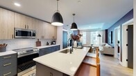 Located at 2902 N Arthur Ashe Blvd in Richmond, VA, this thoughtfully designed 2-bedroom, 2-bathroom residence offers a refined modern aesthetic across a well-appointed single-floor layout. The open-concept kitchen and living area serves as the heart of the home, anchored by a large center island with a quartz countertop and undermount sink, dual pendant lighting, and two-tone cabinetry — pairing light wood uppers with slate-blue lowers accented by gold hardware. A white subway tile backsplash and stainless steel appliances complete the contemporary kitchen. The living room impresses with a bold burgundy accent wall, large windows that invite natural light and urban views, and light wood-look flooring that flows throughout the common areas. The primary bedroom features plush carpeting, a ceiling fan, and charcoal-toned double doors leading to a dedicated closet. Its en-suite bathroom showcases navy cabinetry with gold pulls, a white quartz vanity, and warm gray walls. The second bedroom offers a dramatic dark palette with generous window views of the surrounding cityscape. The second bathroom features a tub-shower combination, light wood flooring, and a sleek floating vanity with gold accents, maintaining the home's cohesive modern design language.