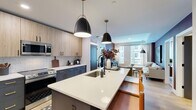 Located at 2902 N Arthur Ashe Blvd in Richmond, VA, this thoughtfully designed 2-bedroom, 2-bathroom residence offers a refined modern aesthetic across a well-appointed single-floor layout. The open-concept kitchen and living area serves as the heart of the home, anchored by a large center island with a quartz countertop and undermount sink, dual pendant lighting, and two-tone cabinetry — pairing light wood uppers with slate-blue lowers accented by gold hardware. A white subway tile backsplash and stainless steel appliances complete the contemporary kitchen. The living room impresses with a bold burgundy accent wall, large windows that invite natural light and urban views, and light wood-look flooring that flows throughout the common areas. The primary bedroom features plush carpeting, a ceiling fan, and charcoal-toned double doors leading to a dedicated closet. Its en-suite bathroom showcases navy cabinetry with gold pulls, a white quartz vanity, and warm gray walls. The second bedroom offers a dramatic dark palette with generous window views of the surrounding cityscape. The second bathroom features a tub-shower combination, light wood flooring, and a sleek floating vanity with gold accents, maintaining the home's cohesive modern design language.